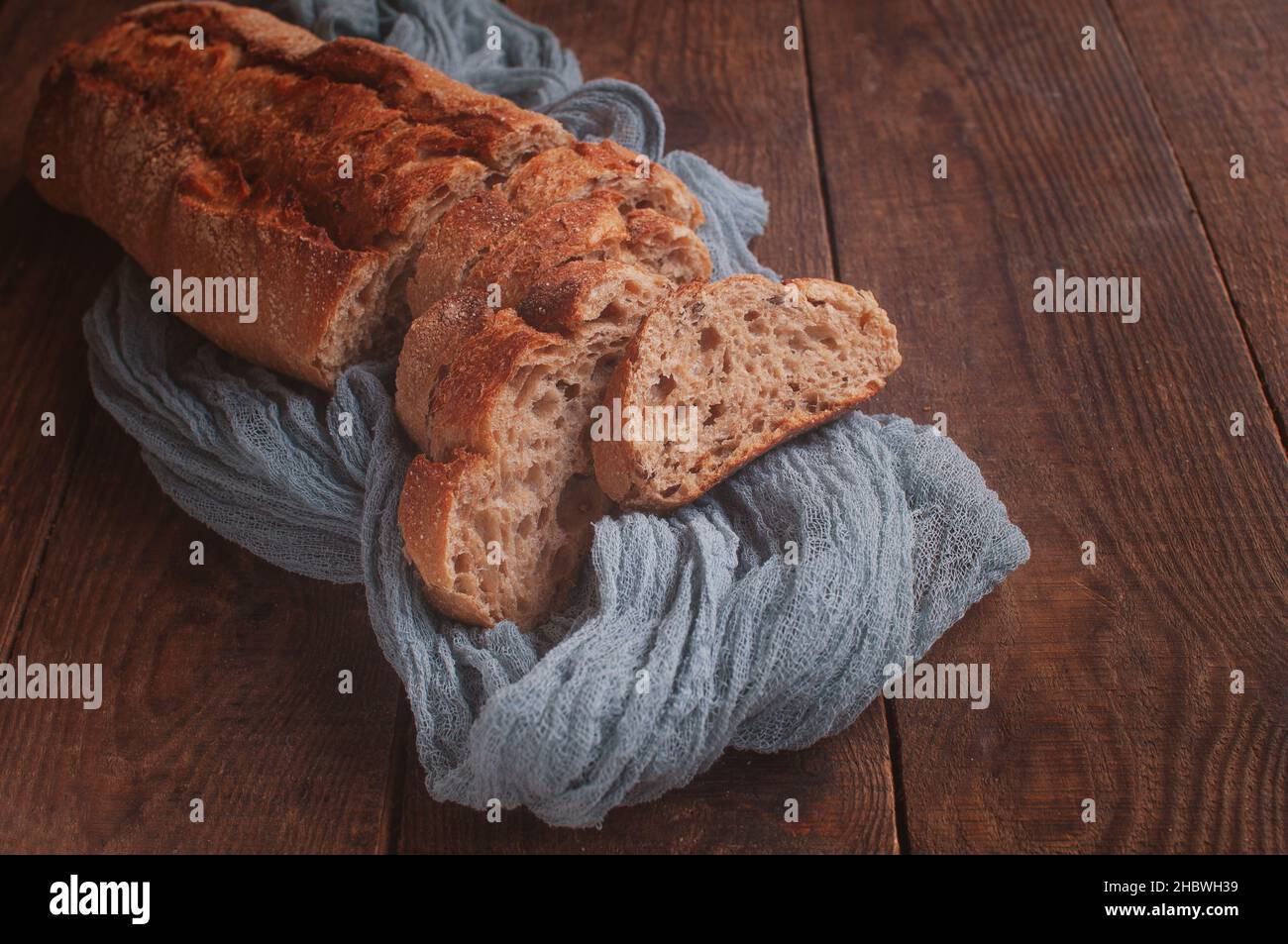 Brotscheiben auf einem Holztisch mit einer grauen Gaze-Tischdecke, frisches Baguette auf einem Holzhintergrund Stockfoto