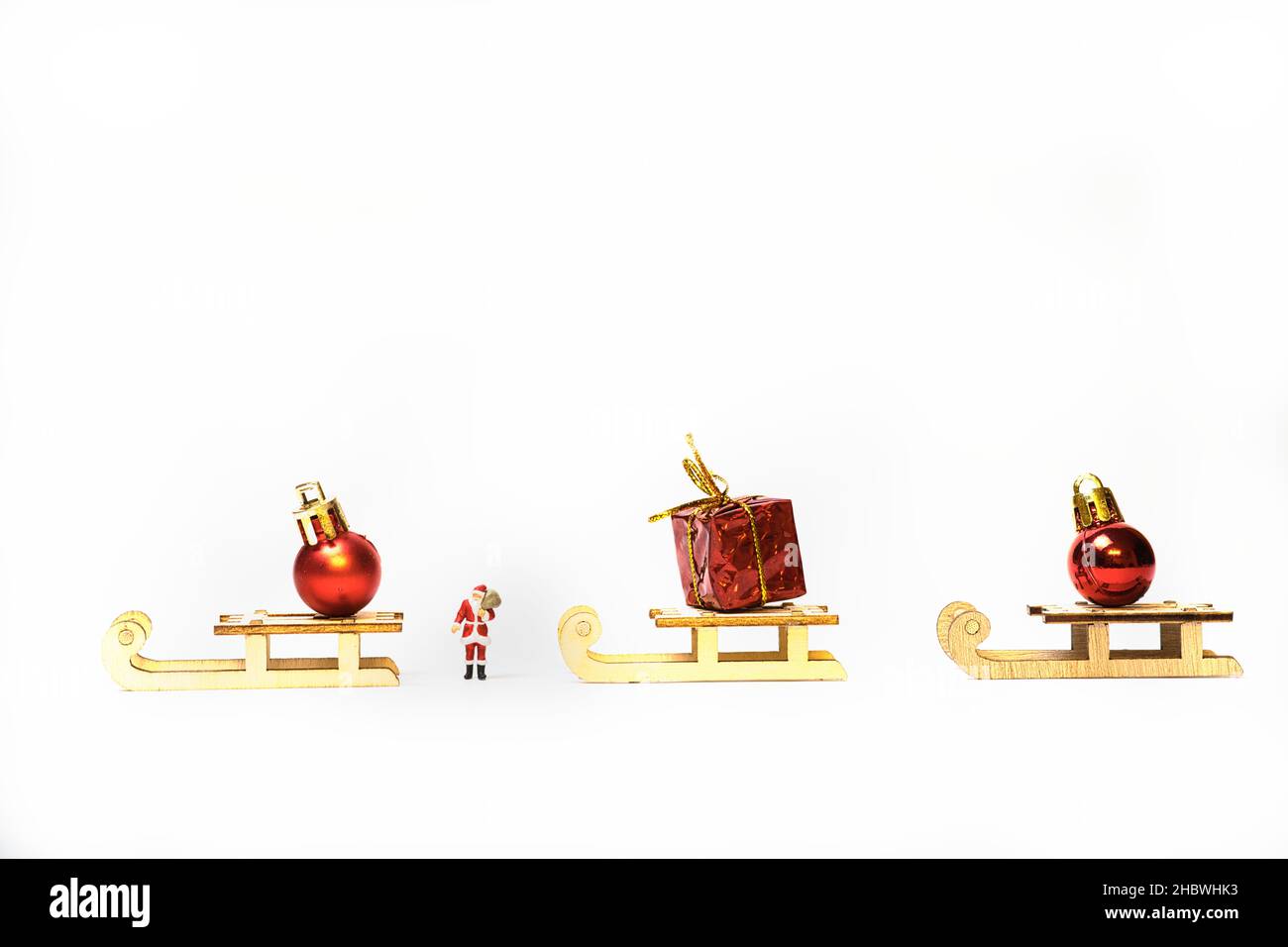 Ein Miniatur-Weihnachtsmann zwischen Schlitten mit Geschenkpaketen und Weihnachtsbaumkugeln Stockfoto