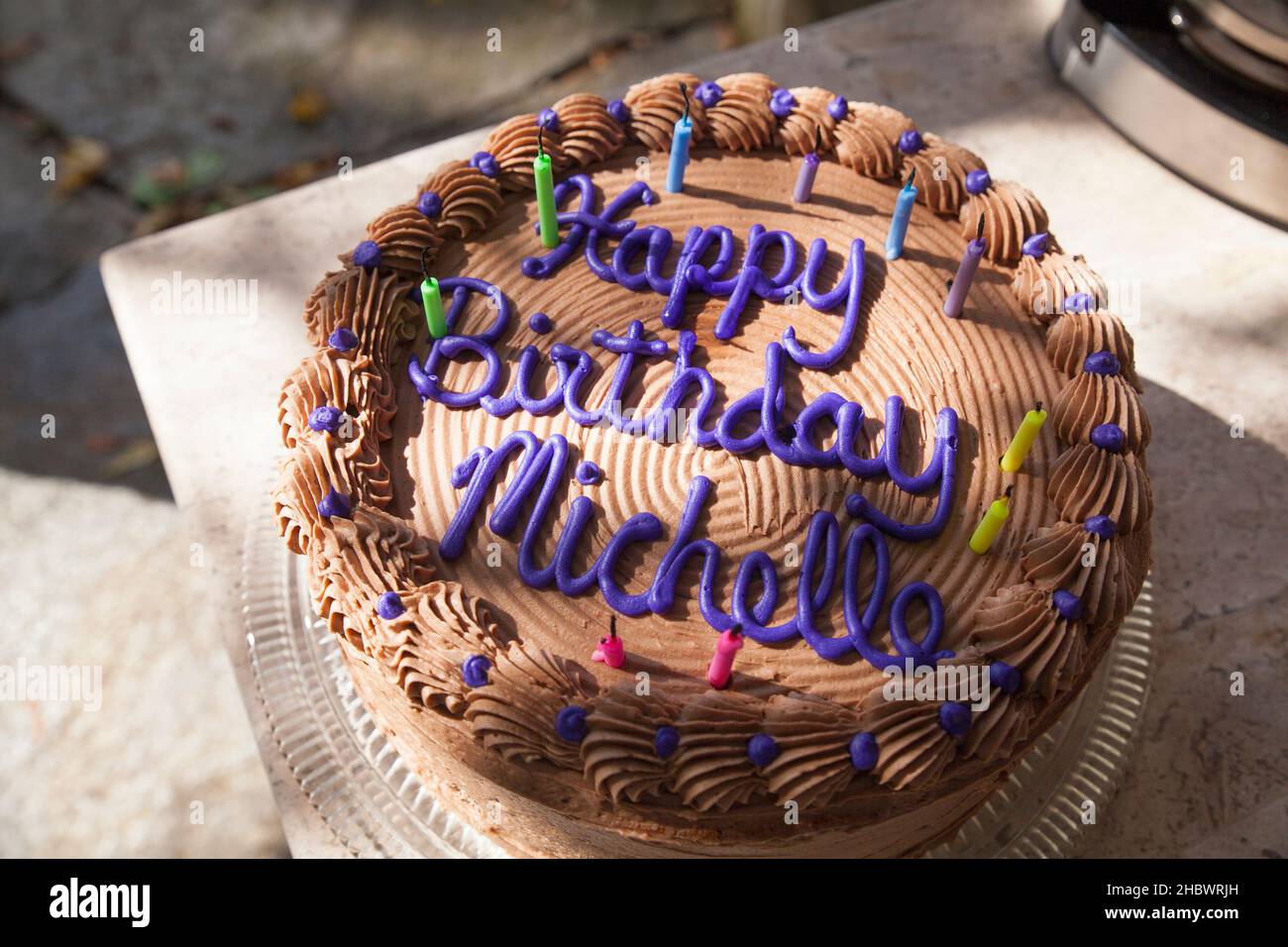 Schokoladenkuchen zum Geburtstag mit verbrannten Kerzen im gefilterten Sonnenlicht draußen. Stockfoto