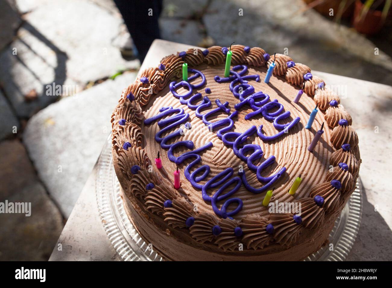Schokoladenkuchen zum Geburtstag mit verbrannten Kerzen im gefilterten Sonnenlicht draußen. Stockfoto