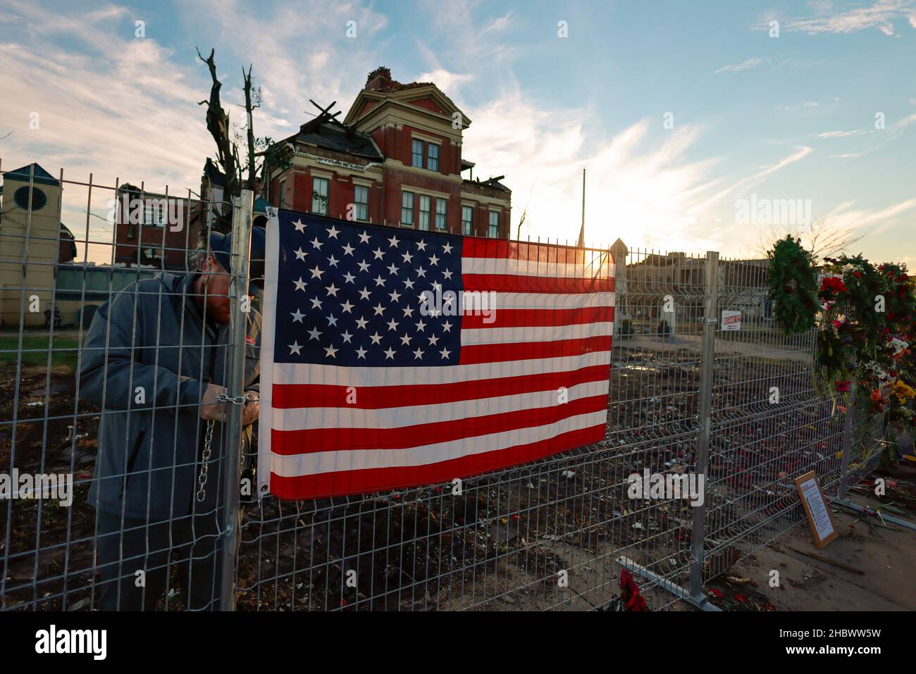 MAYFIELD, KENTUCKY - 20. DEZEMBER: Arbeiter sperren Tor hinter amerikanischer Flagge am provisorischen Denkmal auf einem Zaun um das Graves County Gerichtsgebäude, am 20. Dezember 2021 in Mayfield, Kentucky. Mehrere nächtliche Tornados schlugen am 10. Dezember in mehreren Bundesstaaten des Mittleren Westens ein, was zu weit verbreiteten Zerstörungen und mehreren Verletzten führte. Stockfoto