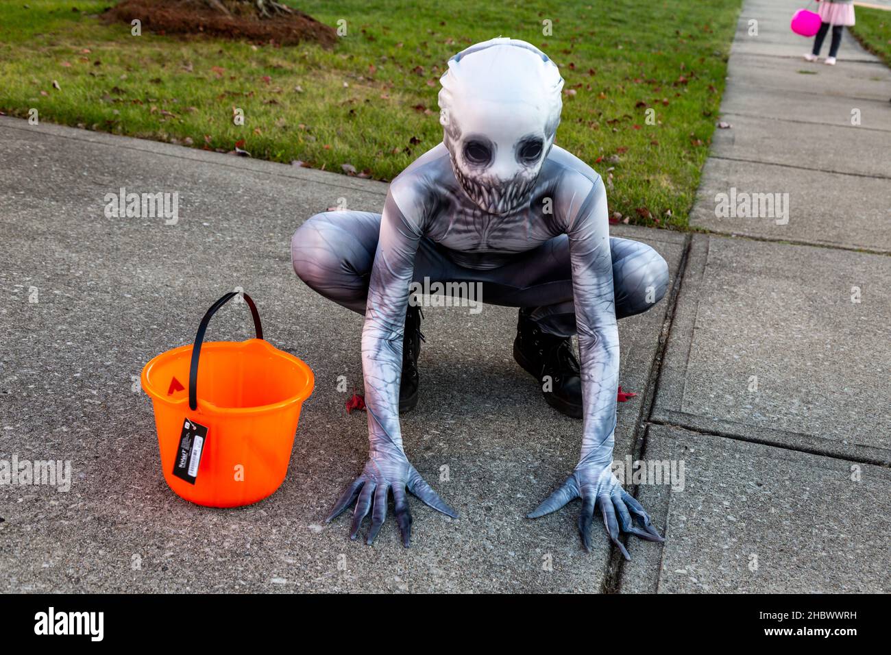 Ein junger Trick oder Treater hockt auf der Auffahrt, als er Halloween in einem gruseligen Zentai Zombie Kostüm feiert. Stockfoto
