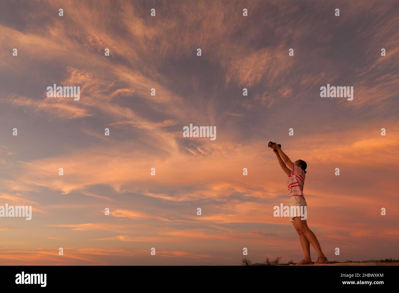 Die Amateurfotografin hebt ihre Kamera, um den farbenfrohen Himmel in der Dämmerung einzufangen Stockfoto