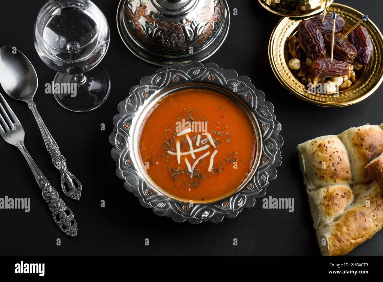 FastenRamadan-Tisch mit Tomatensuppe, Wasser, Dattobst und geschnittenem Ramadan-Brot auf schwarzer Oberfläche. Draufsicht. Stockfoto
