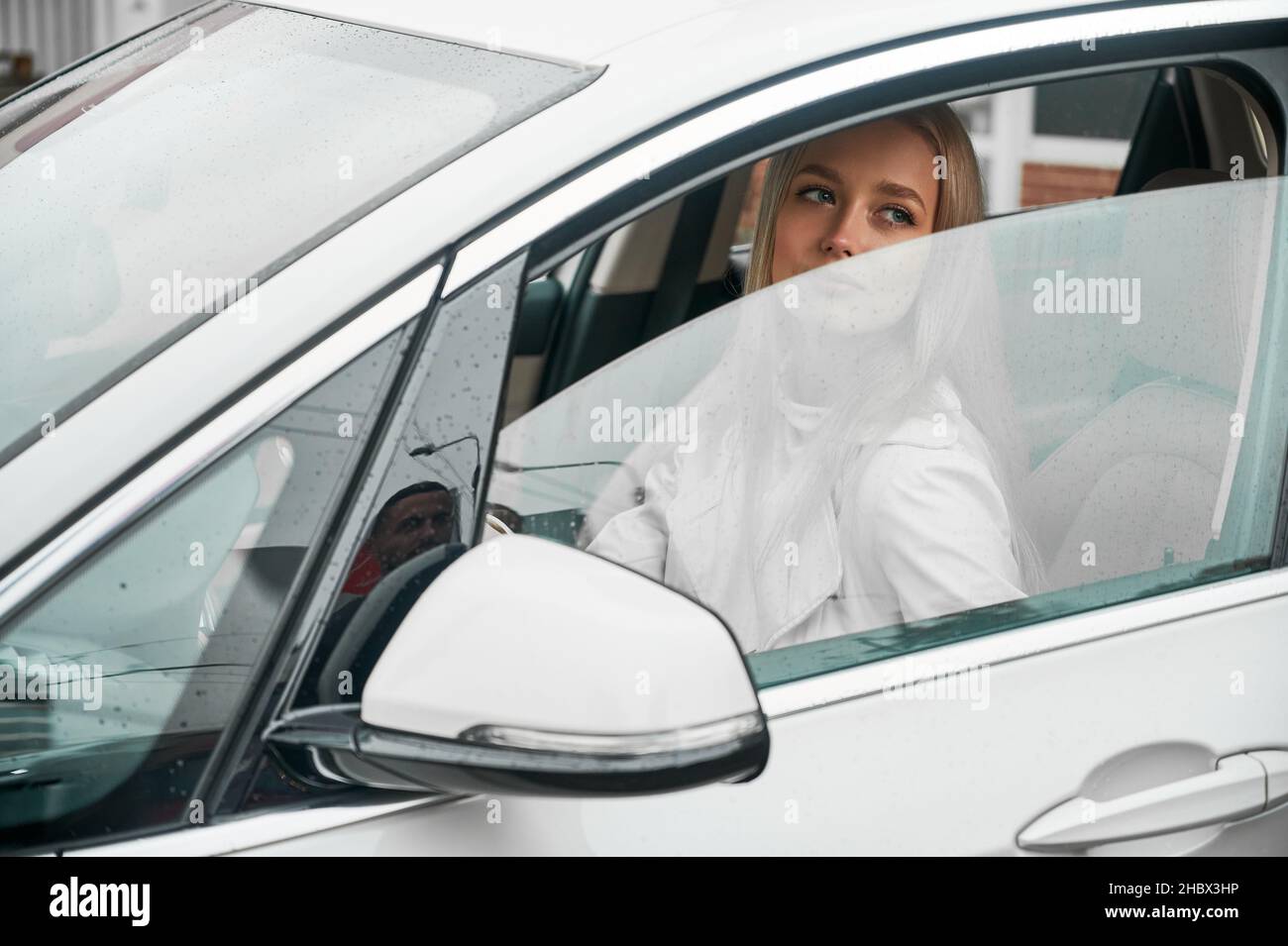Schöne junge Frau, die ein modernes Auto fährt. Weibliche Fahrerin sitzt im Auto und schließt das Fenster. Stockfoto
