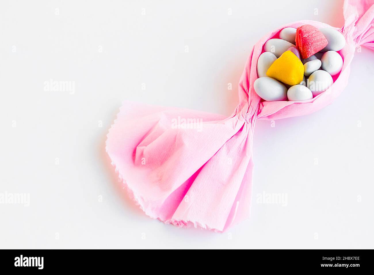 Konzeptuelles Bild mit pinkfarbener Papierbonbon-Form, Mandel-Bonbons in, auf der weißen Oberfläche mit Kopierraum. Stockfoto