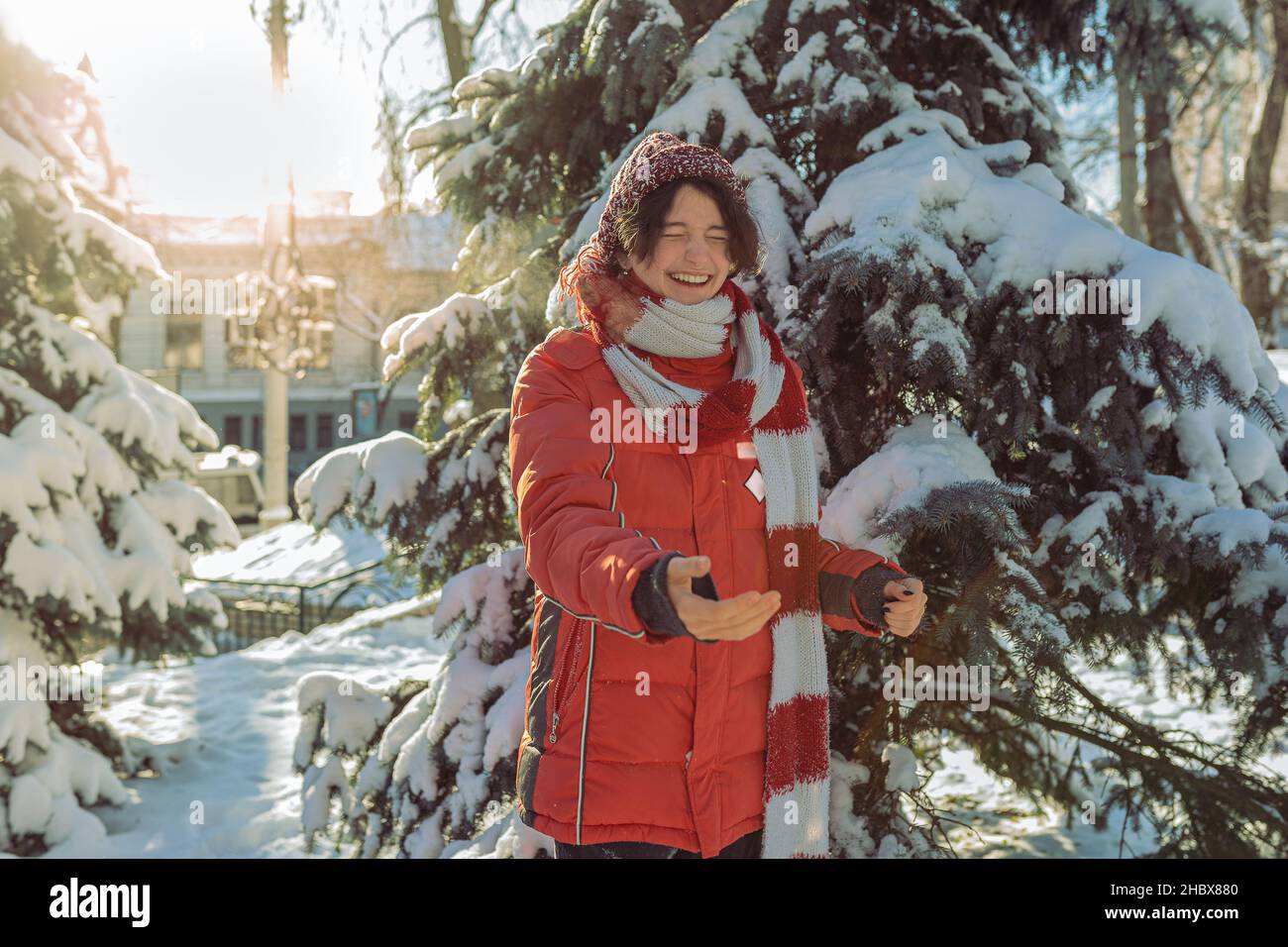 Fröhlich lachende Teenager-Mädchen im Winter warme Kleidung wirft Schnee und spielt im Winter Park bei sonnigem frostigen Wetter Stockfoto