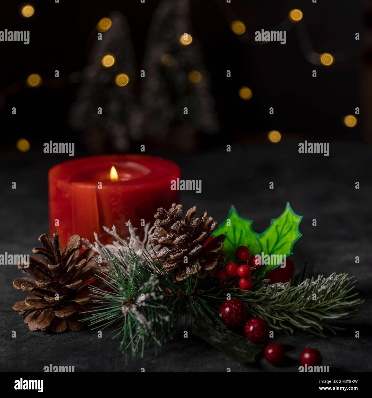 Weihnachtsdekoration mit einer brennenden roten Kerze und Bokeh-Lichterketten im Hintergrund Stockfoto