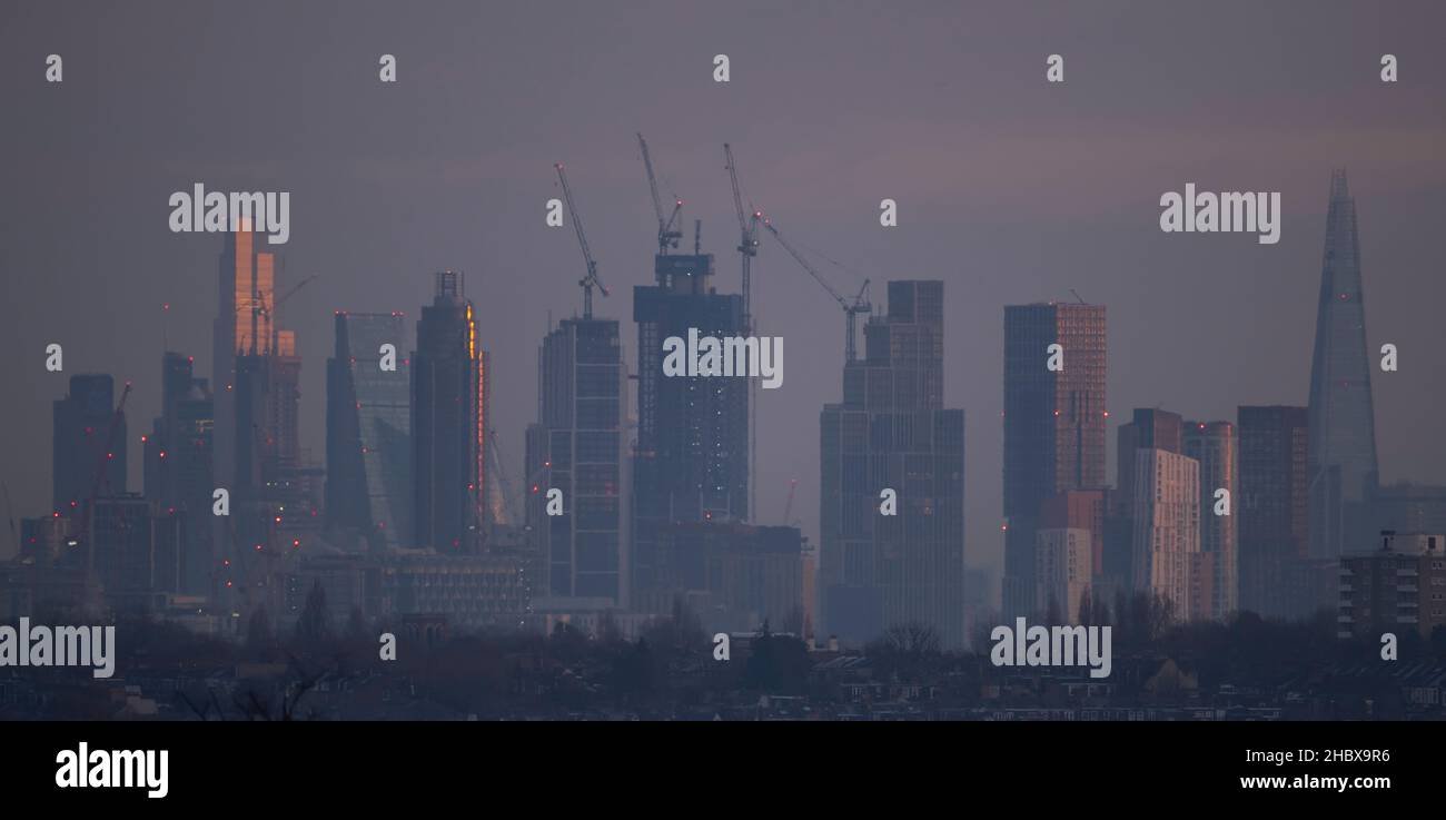 London, Großbritannien. 22. Dezember 2021. Wechselnde Lichtverhältnisse auf Londoner Wolkenkratzern während eines farbenfrohen Wintersonnenaufgangs, bei dem Sonnenlicht die oberen Stockwerke der höchsten Bürogebäude trifft. Aufsteigendes Sonnenlicht trifft den Gipfel des Bishopsgate aus dem Jahr 22 (links im Bild), dem höchsten Gebäude der City of London. Die Sanierung von Hochhäusern in Vauxhall (in der Mitte) verdeckt allmählich einige der Bürogebäude der Stadt, die von Wimbledon aus gesehen werden. Quelle: Malcolm Park/Alamy Live News Stockfoto