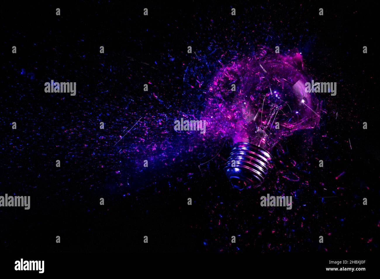 Explosion einer elektrischen Glühbirne auf schwarz. Violettes und blaues Licht. Stockfoto