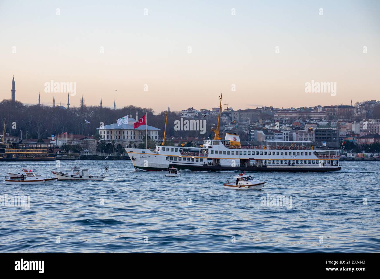 Fischer in Fischerbooten und Linienfähren im Bosporus bei Sonnenaufgang am Wintermorgen in Istanbul, Türkei, am 21. Dezember 2021. Stockfoto