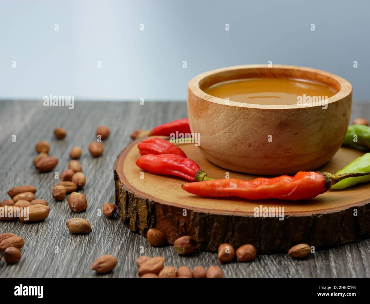 Erdnusssauce in einer kleinen Holzschüssel mit Cayennepfeffer und verstreuten Erdnüssen. Stockfoto