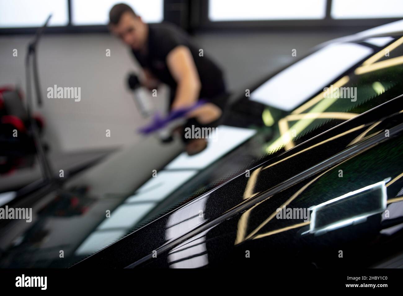 Verschwommener kaukasischer Mann, der die Windschutzscheibe eines Luxuswagens reinigt. Professioneller Arbeiter, in einer Garage. Stockfoto