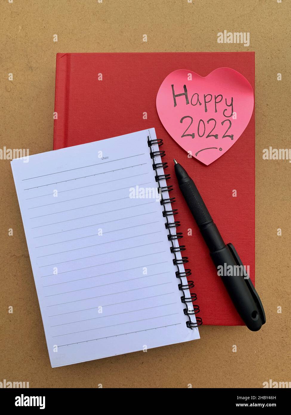 Glückliches Jahr 2022 auf einer Haftnotiz in Form eines Herdes. Rotes Titelbuch, Notizblock und Stifthintergrund. Stockfoto