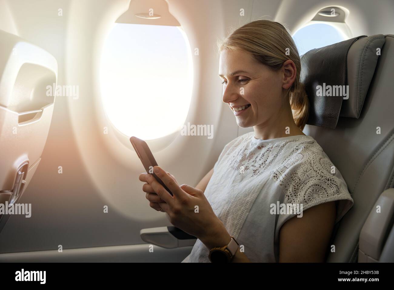 Junge Frau, die während des Fluges im Flugzeug mit dem Mobiltelefon telefoniert Stockfoto