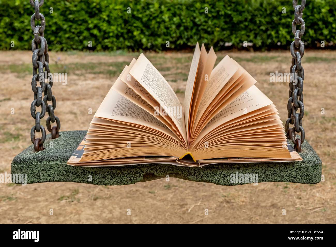 Ein offenes Buch auf dem Sitz einer Schaukel in einem öffentlichen Stadtpark Stockfoto