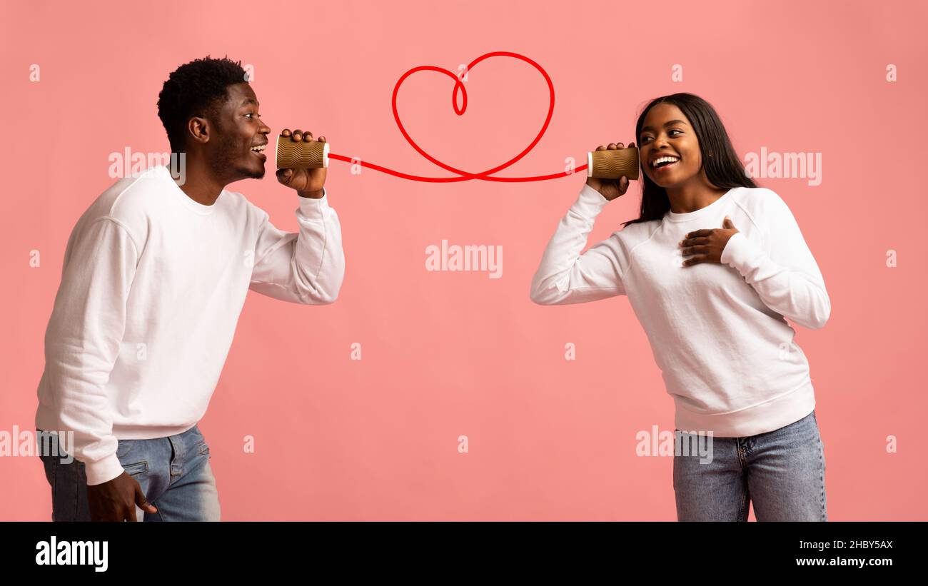Junges schwarzes Paar mit Telefonhörer auf rosa Hintergrund Stockfoto