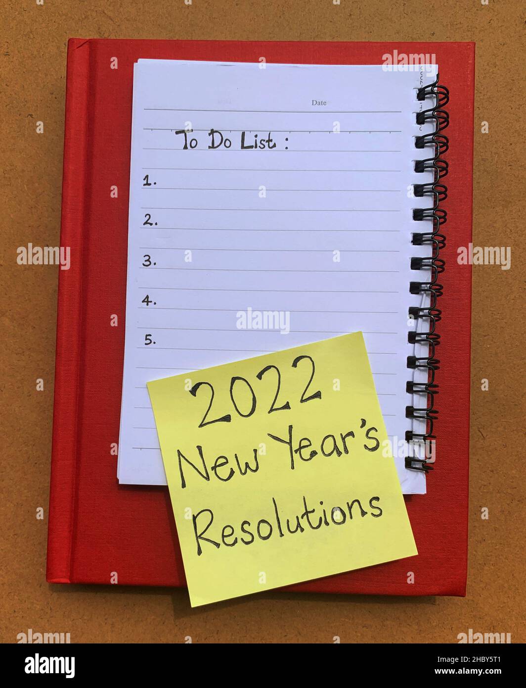 Auf einem Notizblock mit einer Haftnotiz verfasste Liste zu tun, die 2022 neue Jahresvorsätze wünscht. Roter Hintergrund des Buchdeckels Stockfoto