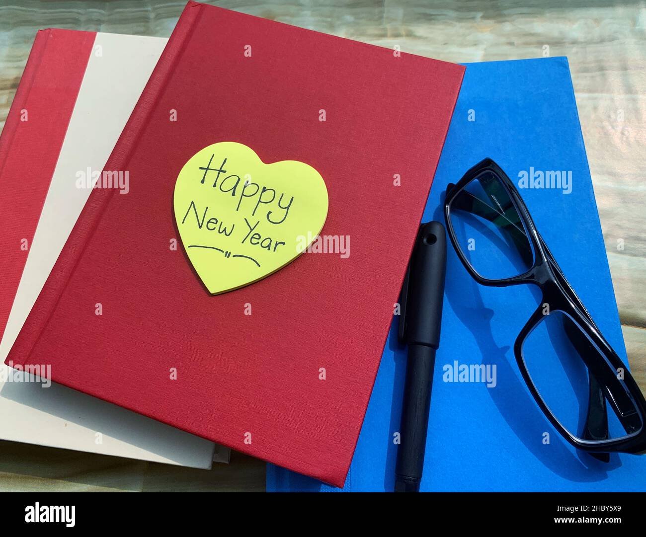 Auf einer herzförmigen Haftnotiz mit Büchern, Stift und Brille sind die Wünsche für das neue Jahr geschrieben. Stockfoto