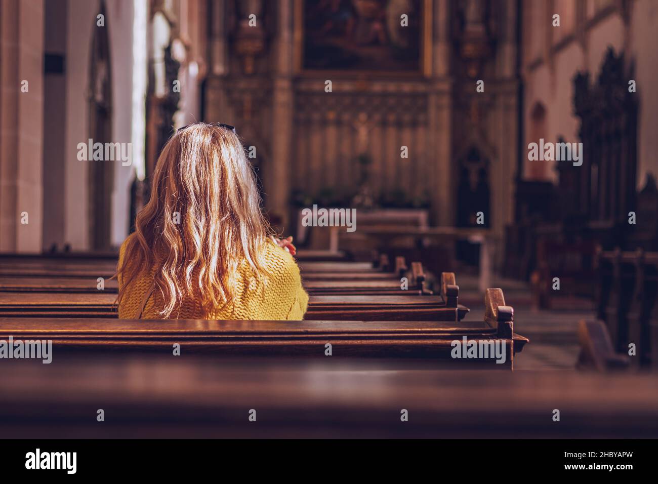 Junge Frau, die in der Kirche betet und meditiert. Glaube an Jesus Christus. Katholische Kathedrale mit Symbol der Religion Stockfoto