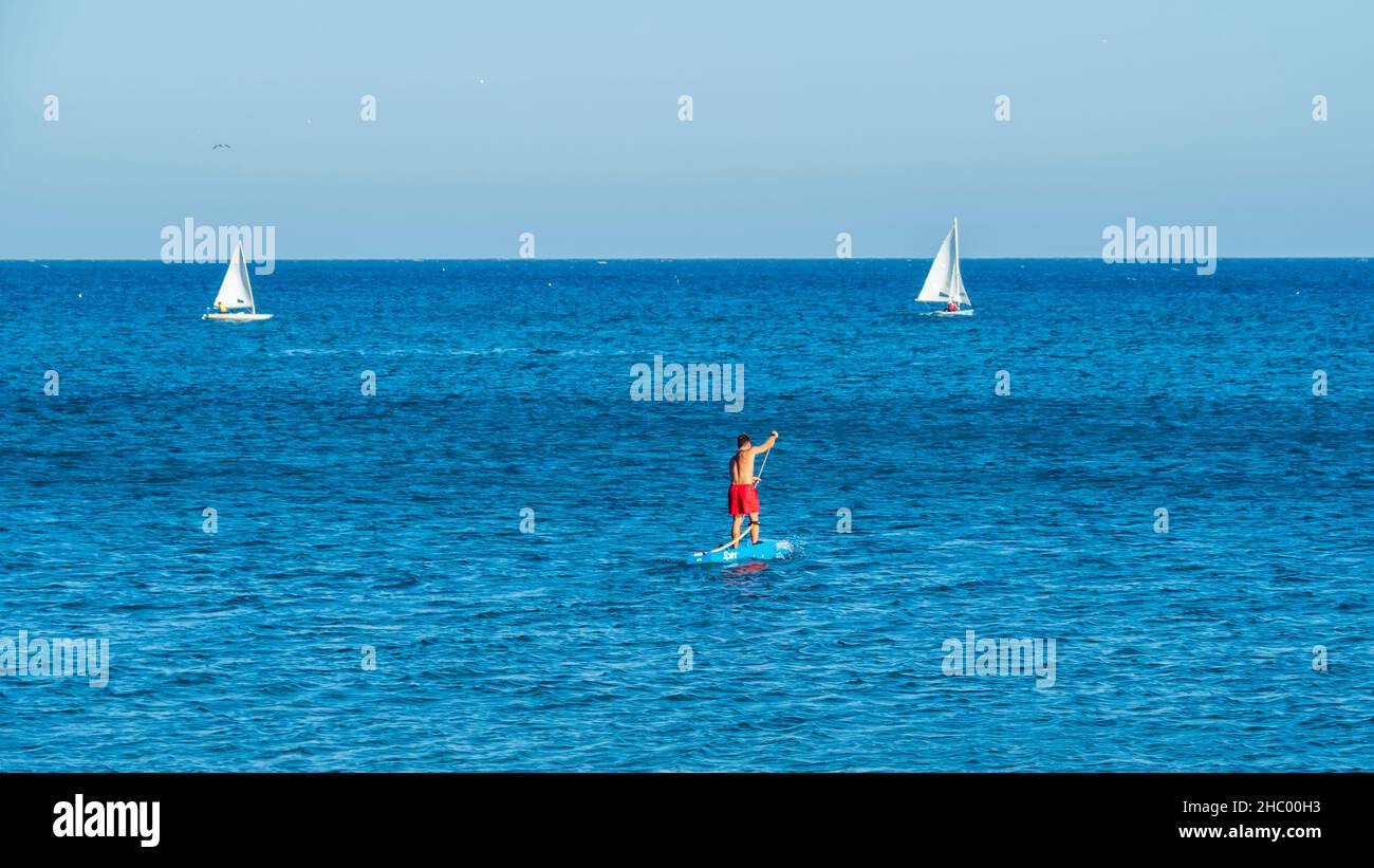 Ein junger Mann in einem roten Schwimmkostüm paddeln im ruhigen Wasser von Fuengirola. Stockfoto