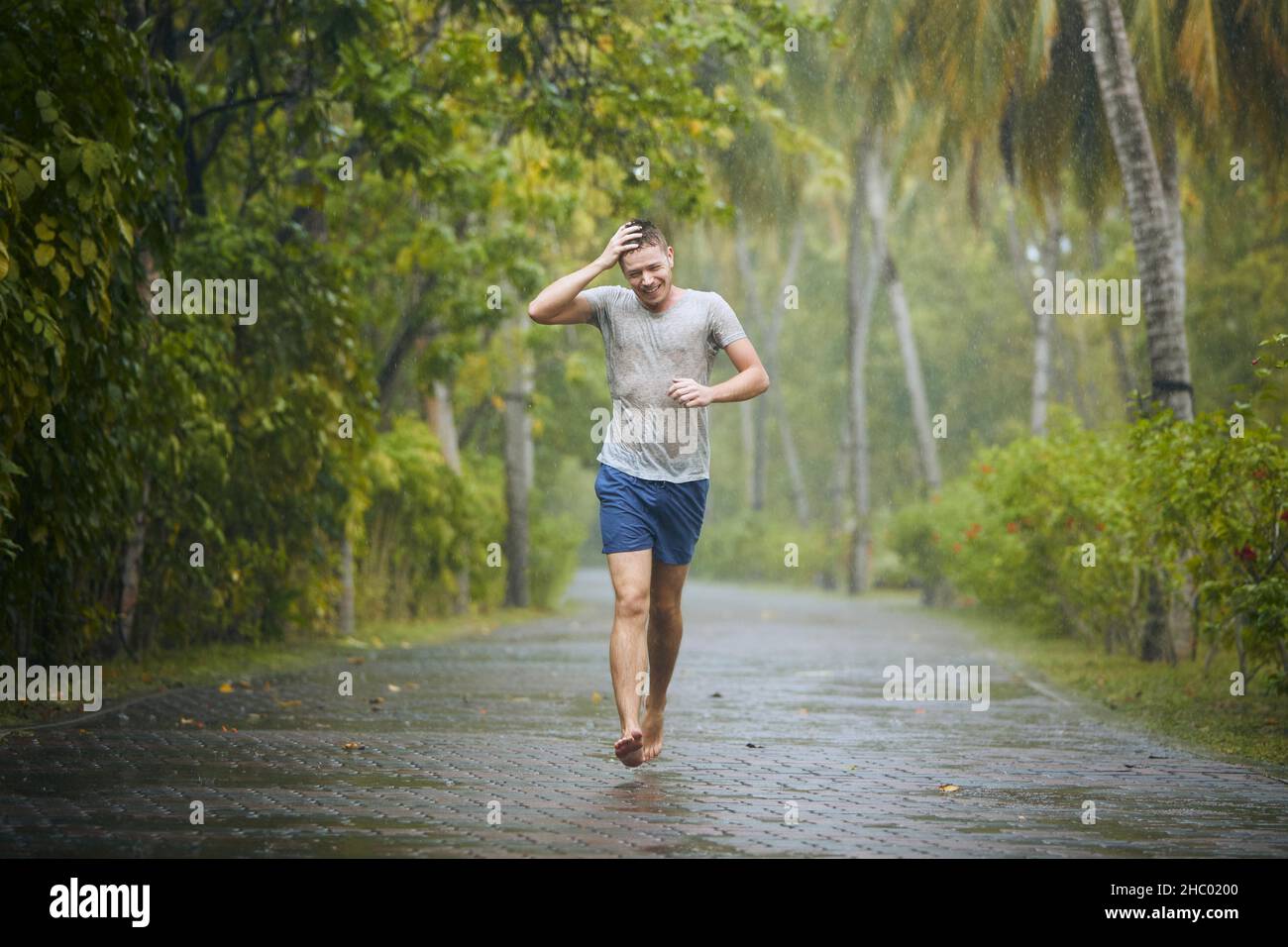 Durchnässt junger Mann, der bei starkem Regen auf der Straße läuft. Stockfoto