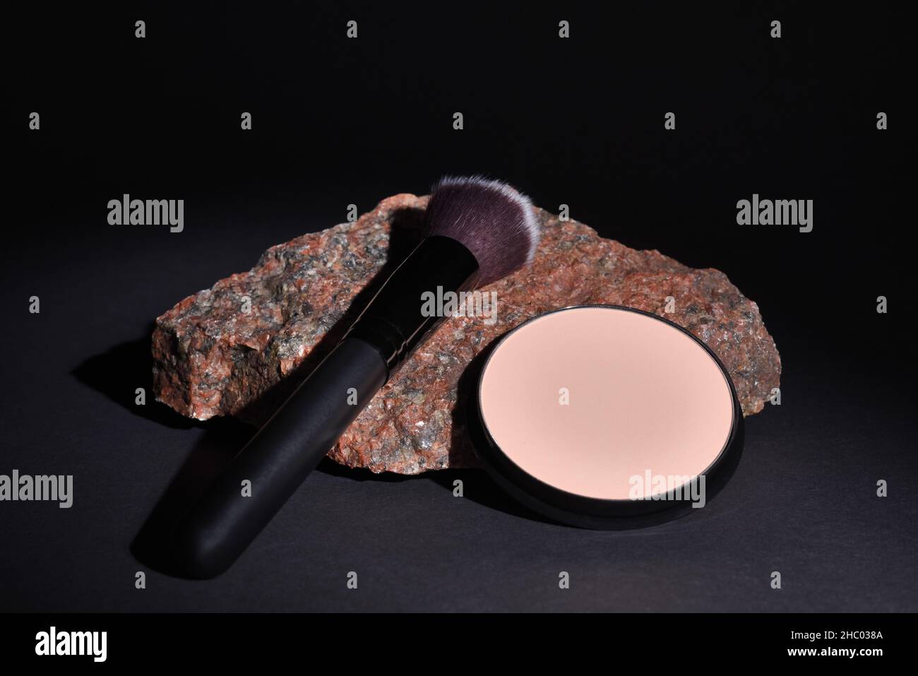 Make-up Pinsel und kompakt gepresstes Pulver liegen auf Granitstein auf schwarzem Hintergrund Stockfoto