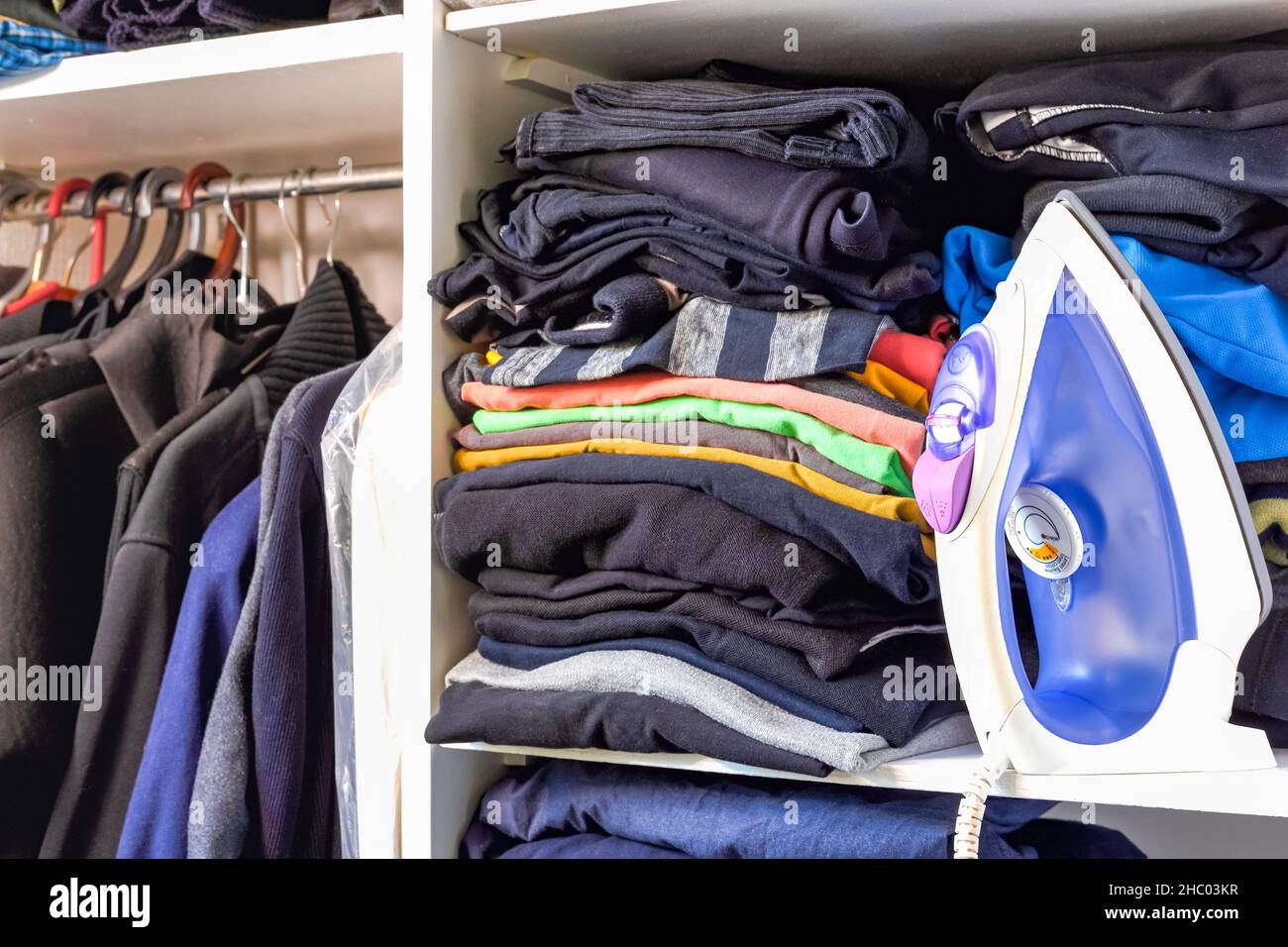 Eisen und ein Stapel gefalteter Herrenmode auf dem Regal. Herrenbekleidung in einem Schrank. Entrümpeln und Reinigen des Hausschranks. Stockfoto