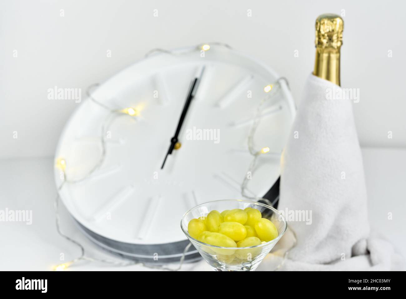 Trauben in einem Glas vor dem Hintergrund einer verschwommenen Uhr und einer Flasche Champagner. Spanische Tradition, zwölf Trauben zu essen, um Neujahr zu feiern. Stockfoto