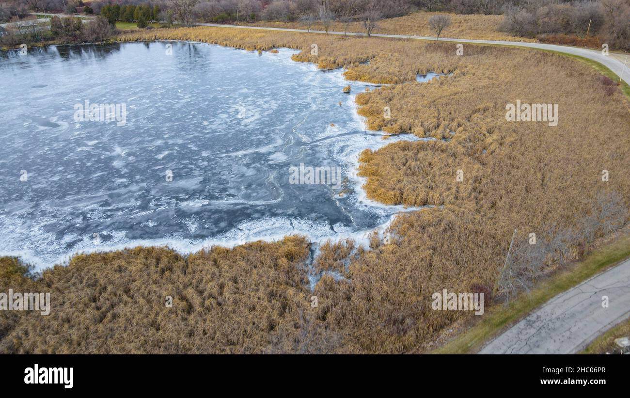 Gefrorenes Wasser an einer kleinen Bucht mit Straße am Rand und Bäumen im Hintergrund. Stockfoto