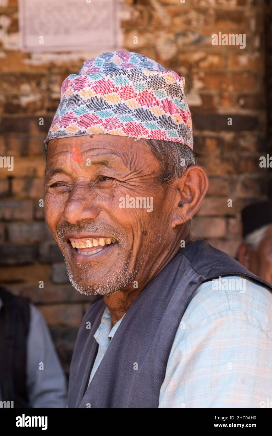In der mittelalterlichen Stadt Bhaktapur in Nepal sitzt ein älterer Nepalesischer Mann mit einer traditionellen Dhaka-Topi-Mütze im Schatten. Stockfoto