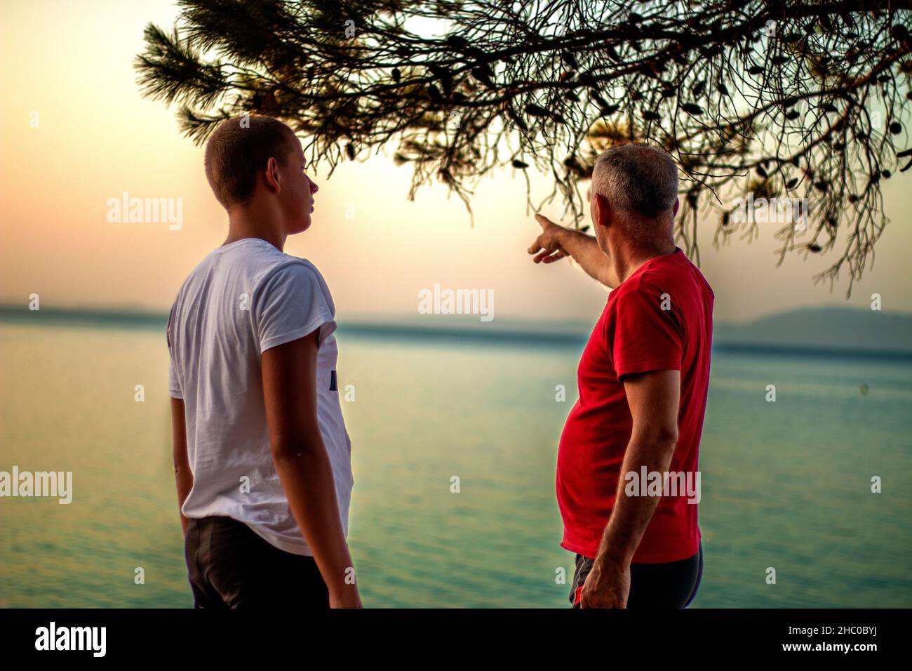 Der Mann zeigt einem Teenager etwas in der Ferne am See Stockfoto