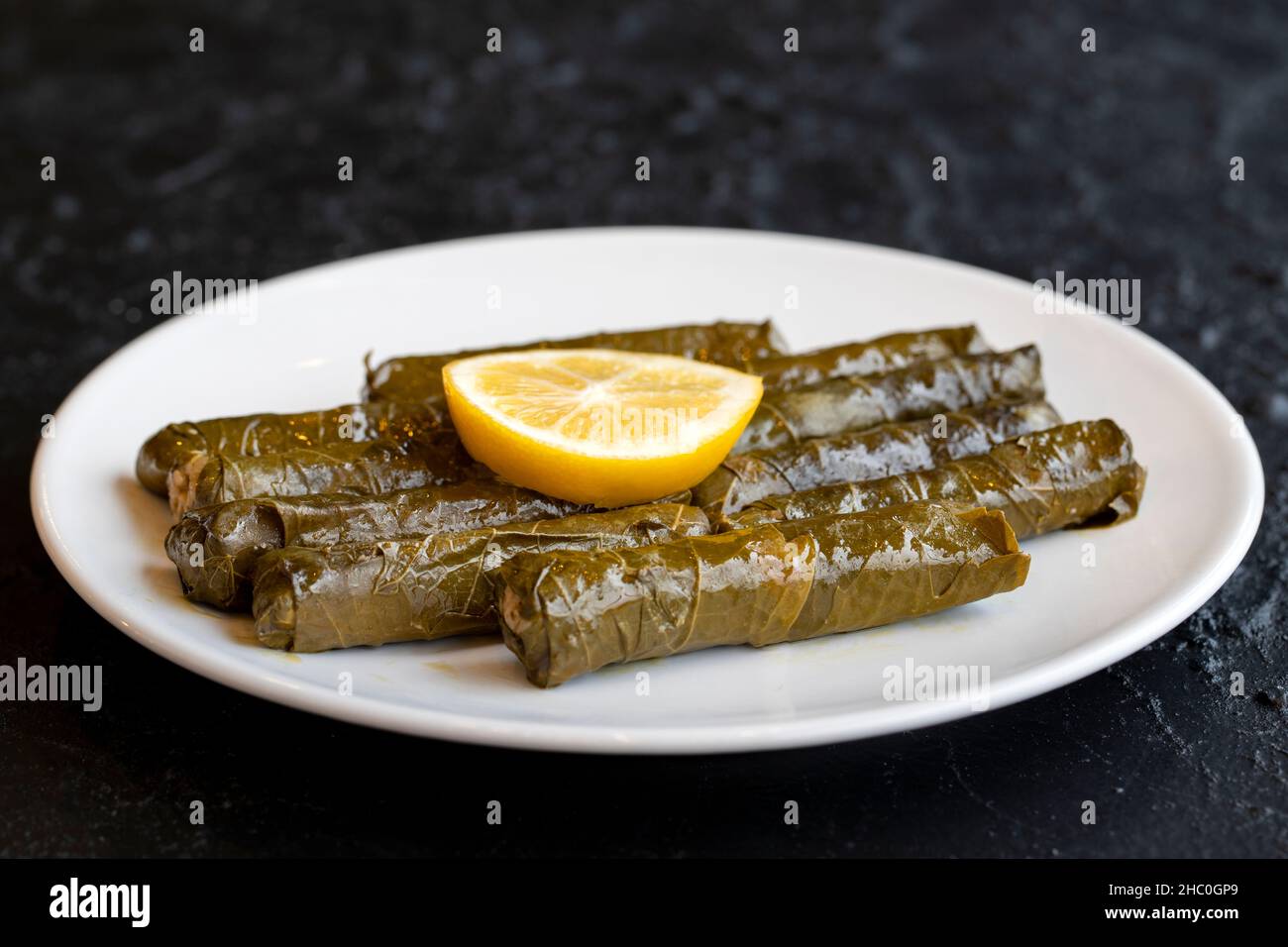 Köstliche Dolma (sarma) gefüllte Traubenblätter Reis, weiße Joghurt-Sauce. Gefüllte Traubenblätter auf dunklem Hintergrund. Libanesischer Dolma-Karma auf dem Teller. Libanon Stockfoto