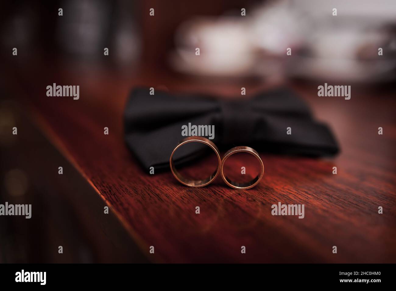 Schwarze Fliege, goldene Hochzeitsringe auf braunem Holzhintergrund Stockfoto