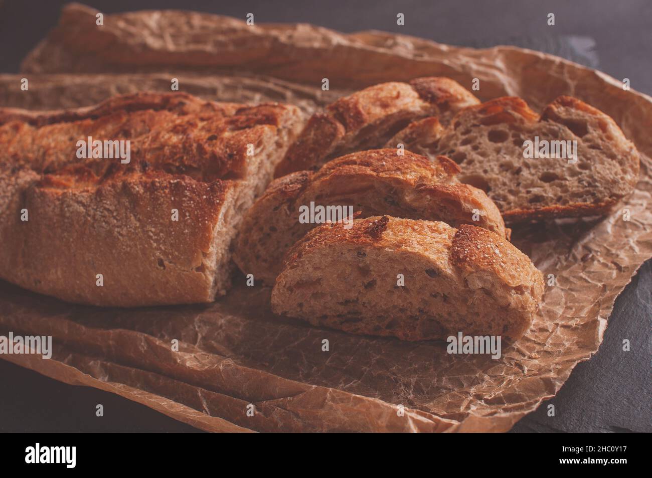Baguette aus Buchweizenmehl ohne Hefe auf schwarzem Hintergrund, Scheiben Brotscheiben auf Pergamentpapier. Stockfoto
