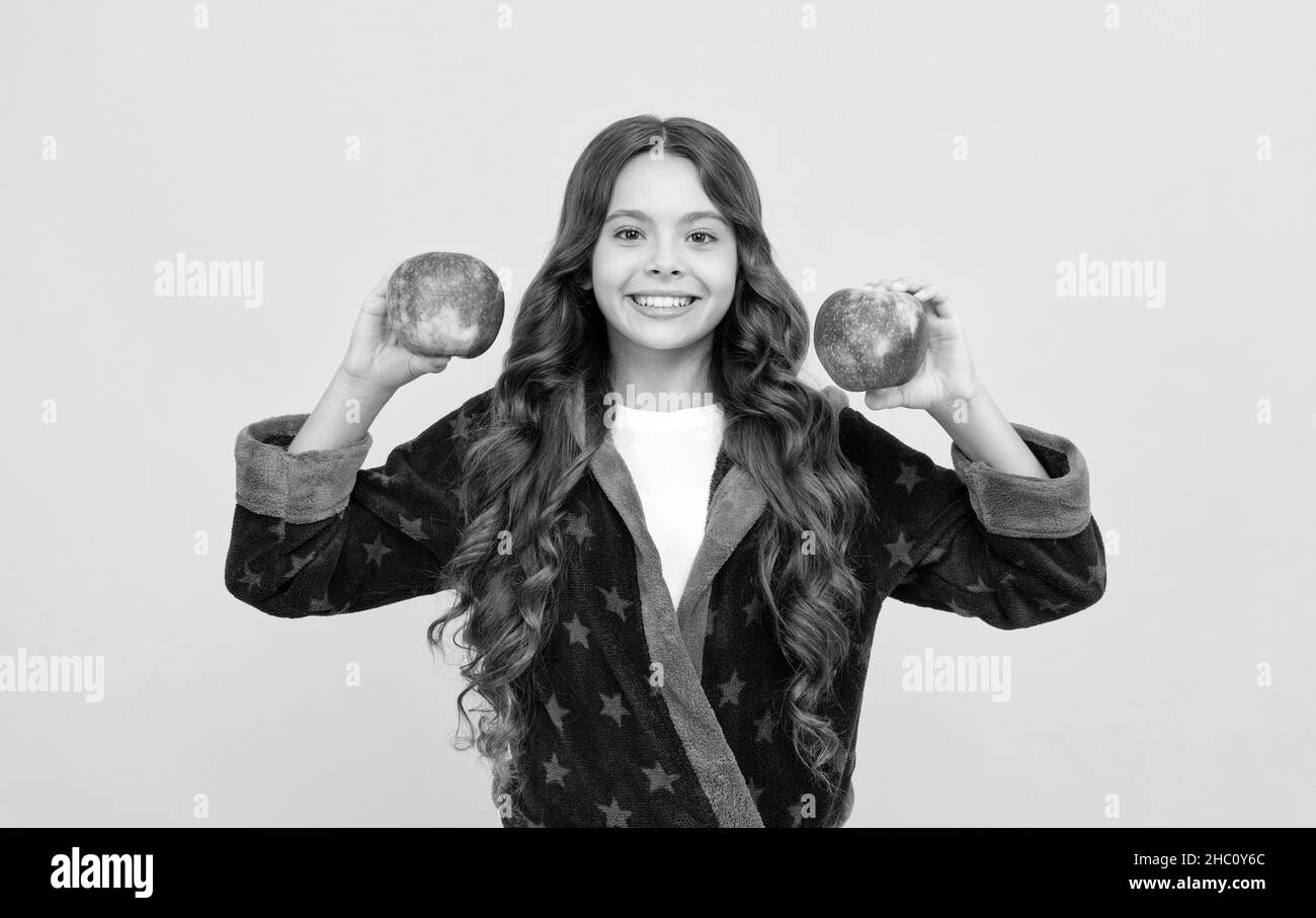 Fröhliche Teenager-Mädchen mit lockigen Haaren in komfortablen Pyjama gehen, um gesunde Apfel, Vitamin essen Stockfoto