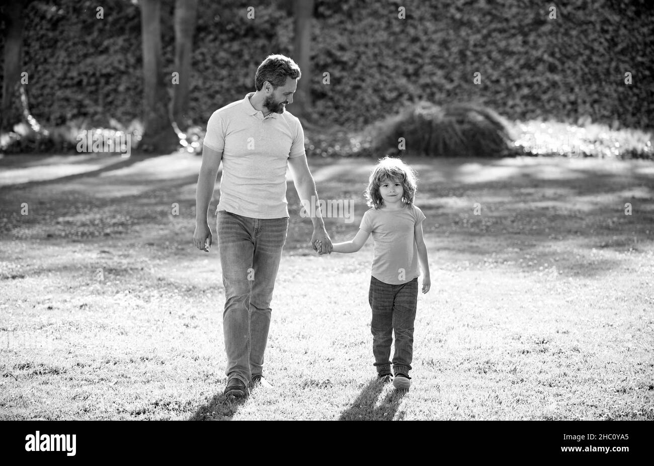 Glücklicher Sohn und Vater halten die Hände zu Fuß an sonnigen Sommertag im Park Gras, Familie Stockfoto