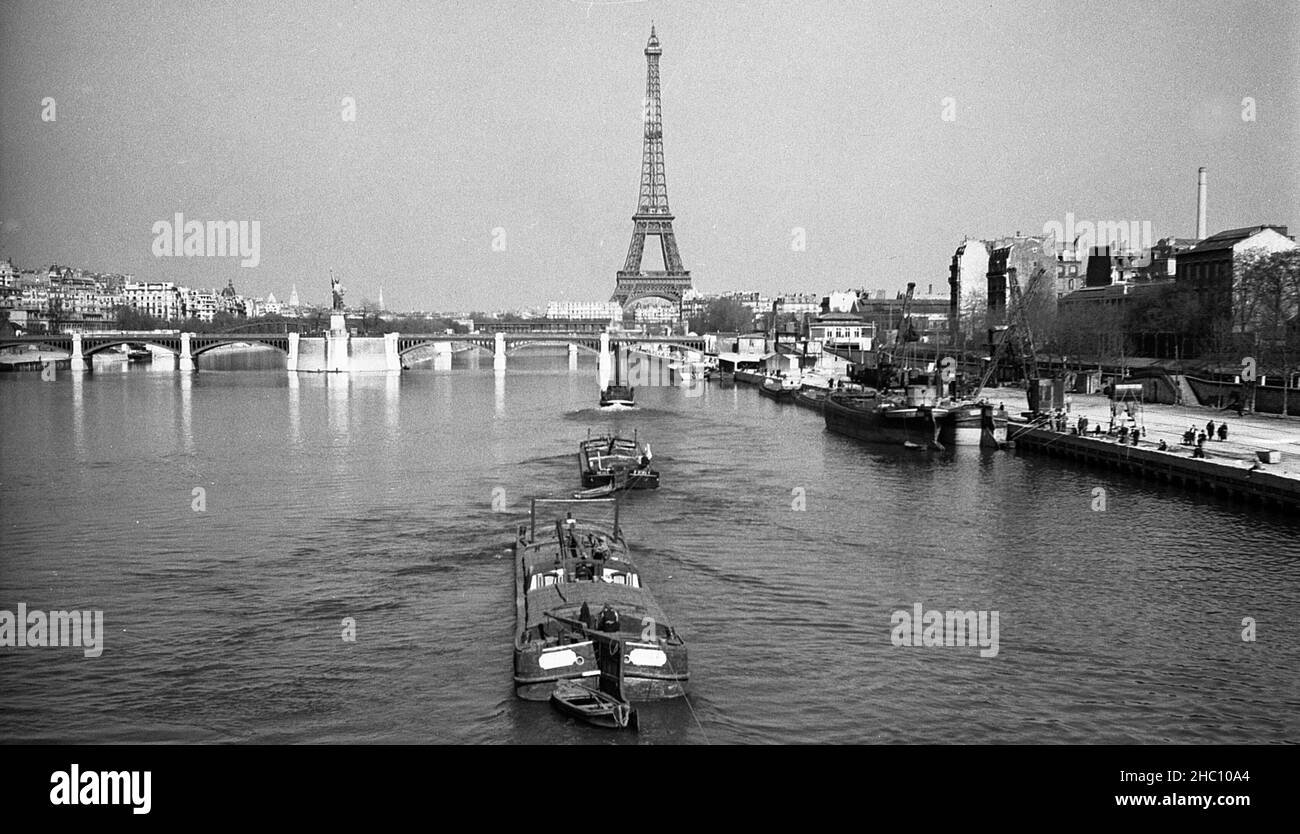 Die seine in Paris führt Schiffe mit der zierlichen Freiheitsstatue und dem Eiffelturm, 1945. Das Bild, das auf der Pont Mirabeau steht, zeigt einen Schleppkahn und zwei Frachtschiffe, die sich von der Kamera wegbewegen. Ein Seil deutet darauf hin, dass andere nicht-Sichtbarren folgen werden. Die zierliche Freiheitsstatue steht vor der Kamera von Pont de Grenelle. Dahinter sind die Pont de Bir Hakeim und der Eiffelturm zu sehen. Stockfoto