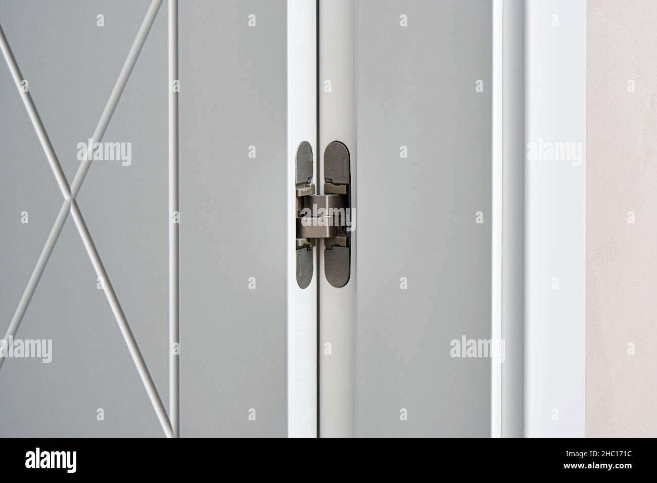 Elegante, moderne weiße Tür mit Rautenmuster, die mit einem Scharnier befestigt ist, das in einem hellen Raum bei der Restaurierung in äußerster Nähe installiert wurde Stockfoto