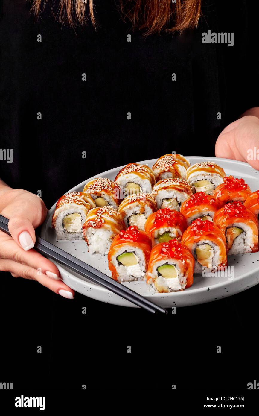 Weibliche Hände halten Essstäbchen und Teller mit Sushi-Rollen mit Lachs und Aal Stockfoto