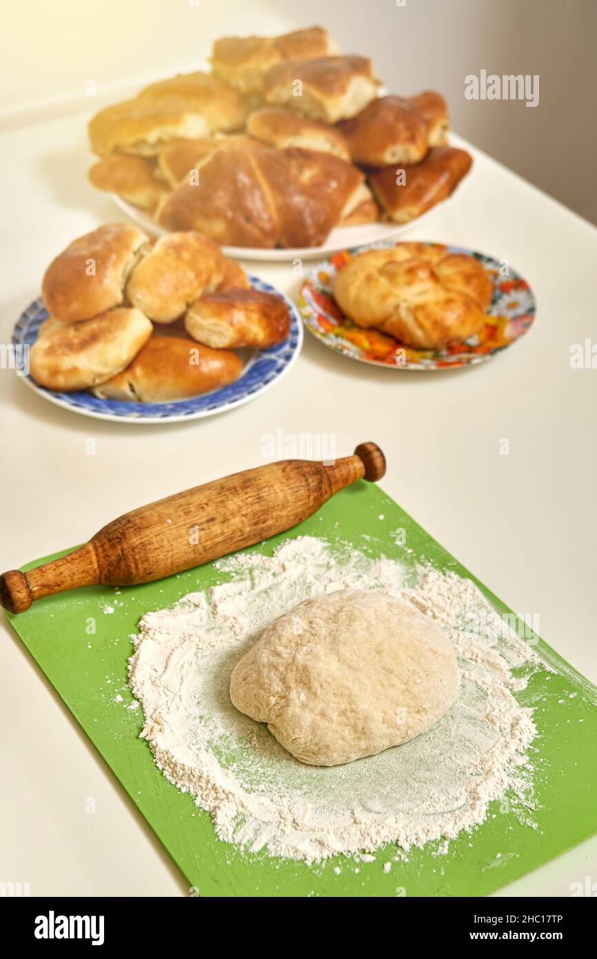 Roher Teig und hölzerne Nudelholz in der Nähe von leckeren frischen hausgemachten süßen und Fleischpasteten auf weißem Tisch in der Küche aus der Nähe Stockfoto