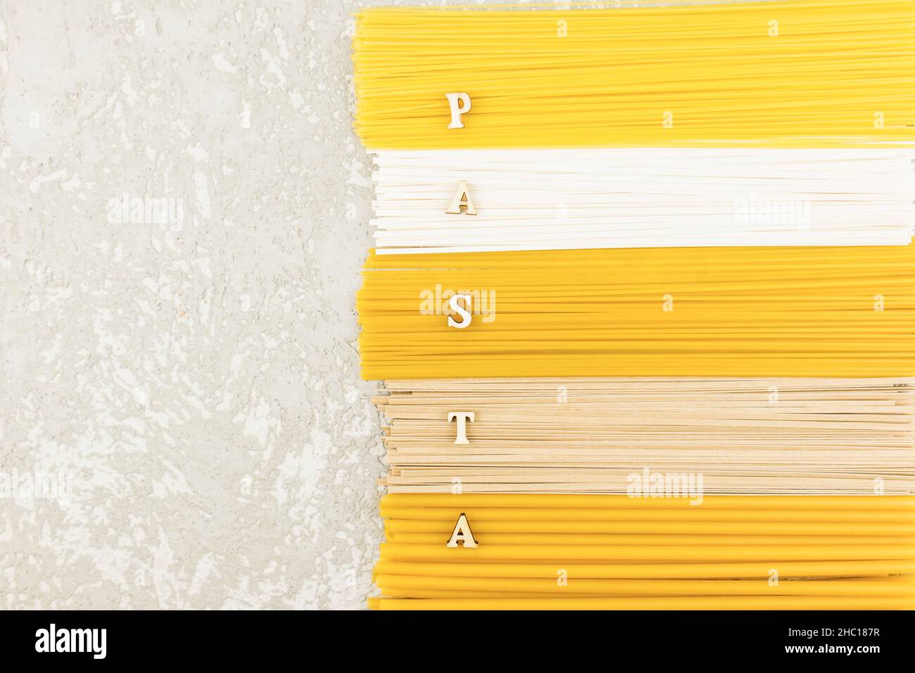 Die Draufsicht auf die trockene italienische Pasta, Nudeln, Spaghetti auf einem grauen Hintergrund mit einer Kopie des Raumes und den Buchstaben des Wortes - Pasta. Flach legen Stockfoto