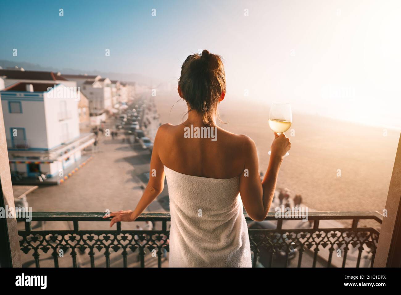 Frau, die auf dem Balkon steht und ein Glas Weißwein in der Hand hält. Genießen Sie das Leben Stockfoto