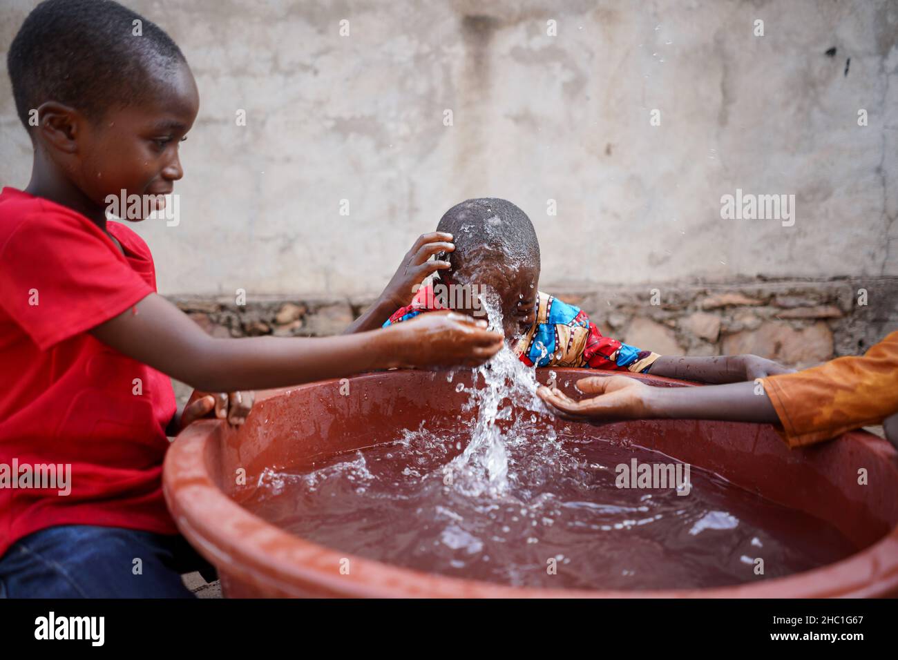 Drei schicke kleine schwarze afrikanische Jungen, die eine tolle Zeit mit frischem Wasser in einer großen Plastikwanne herumplanschen Stockfoto