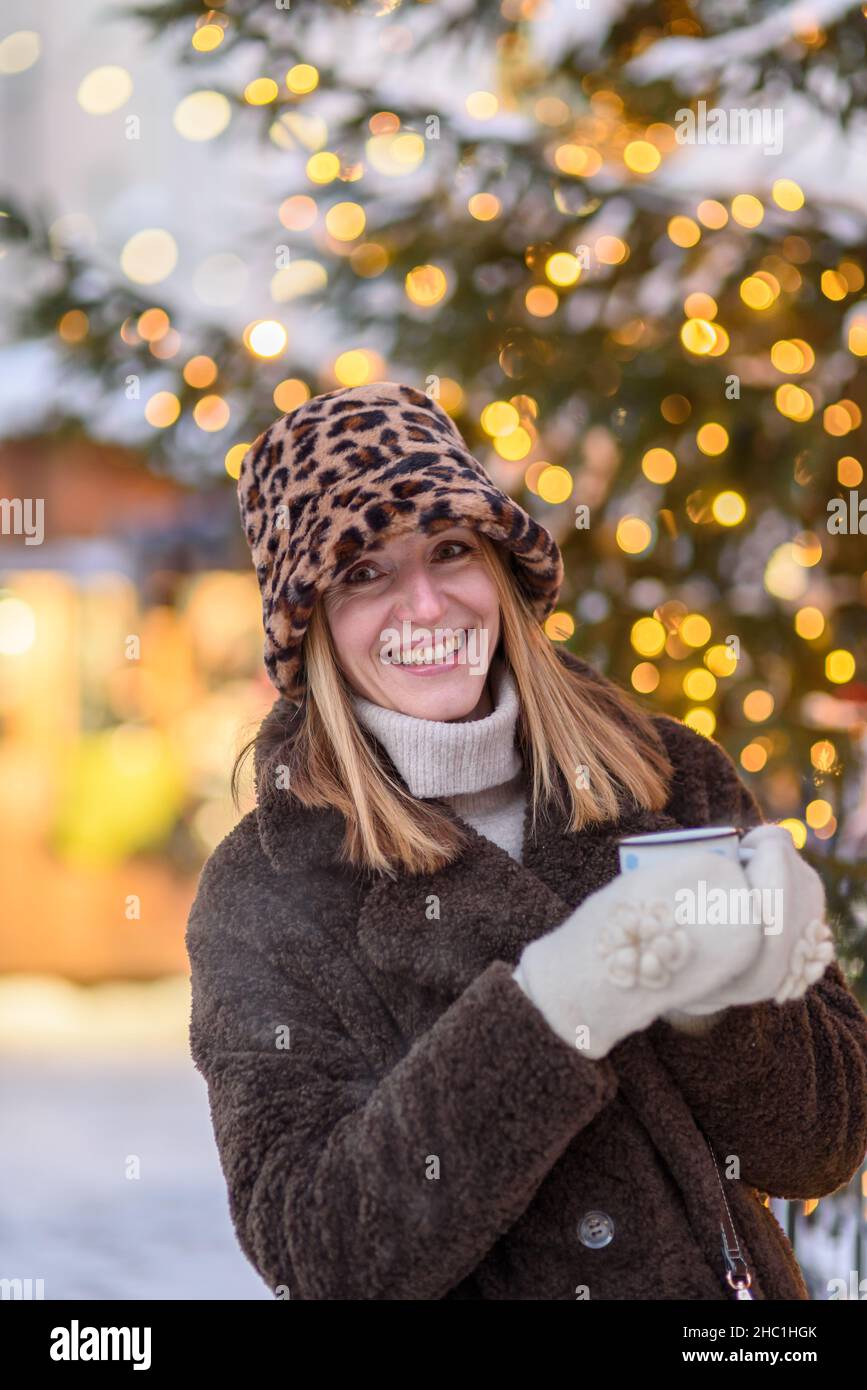 Frau im Pelzmantel, panamahut auf dem Talliner Weihnachtsmarkt, die heißen Glühwein aus einem wiederverwendbaren Becher trinkt Stockfoto