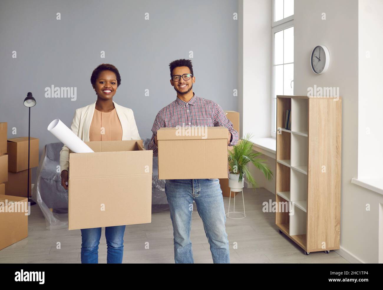 Glückliches, lächelndes junges Paar, das in ein neues Haus zieht und Kartons zusammen trägt Stockfoto