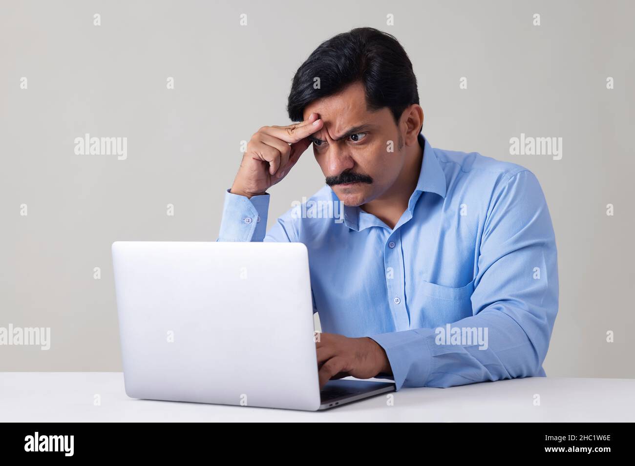 Porträt eines stressigen Mannes, der die Hand auf die Stirn hält, während er mit einem Laptop im Büro arbeitet Stockfoto