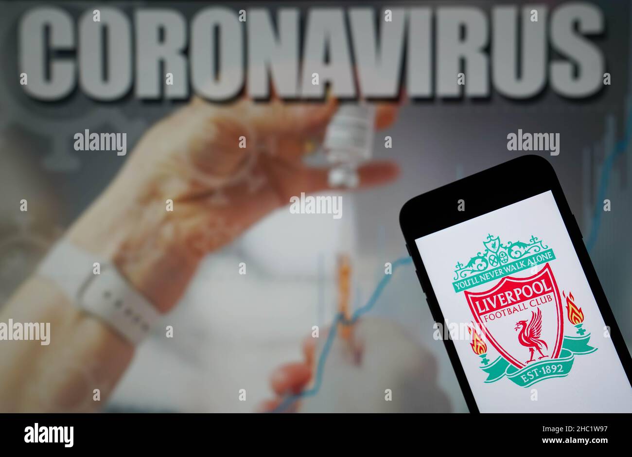 Aktenfoto vom 09-01-2021 des Liverpool Football Club-Logos auf einem Mobiltelefon mit einer Coronavirus-Illustration auf einem Monitor im Hintergrund. Liverpools Spiel gegen Leeds und Wolves Spiel gegen Watford am zweiten Weihnachtsfeiertag wurde aufgrund von Coronavirus-Infektionen abgekündigt, hat die Premier League angekündigt. Ausgabedatum: Donnerstag, 23. Dezember 2021. Stockfoto