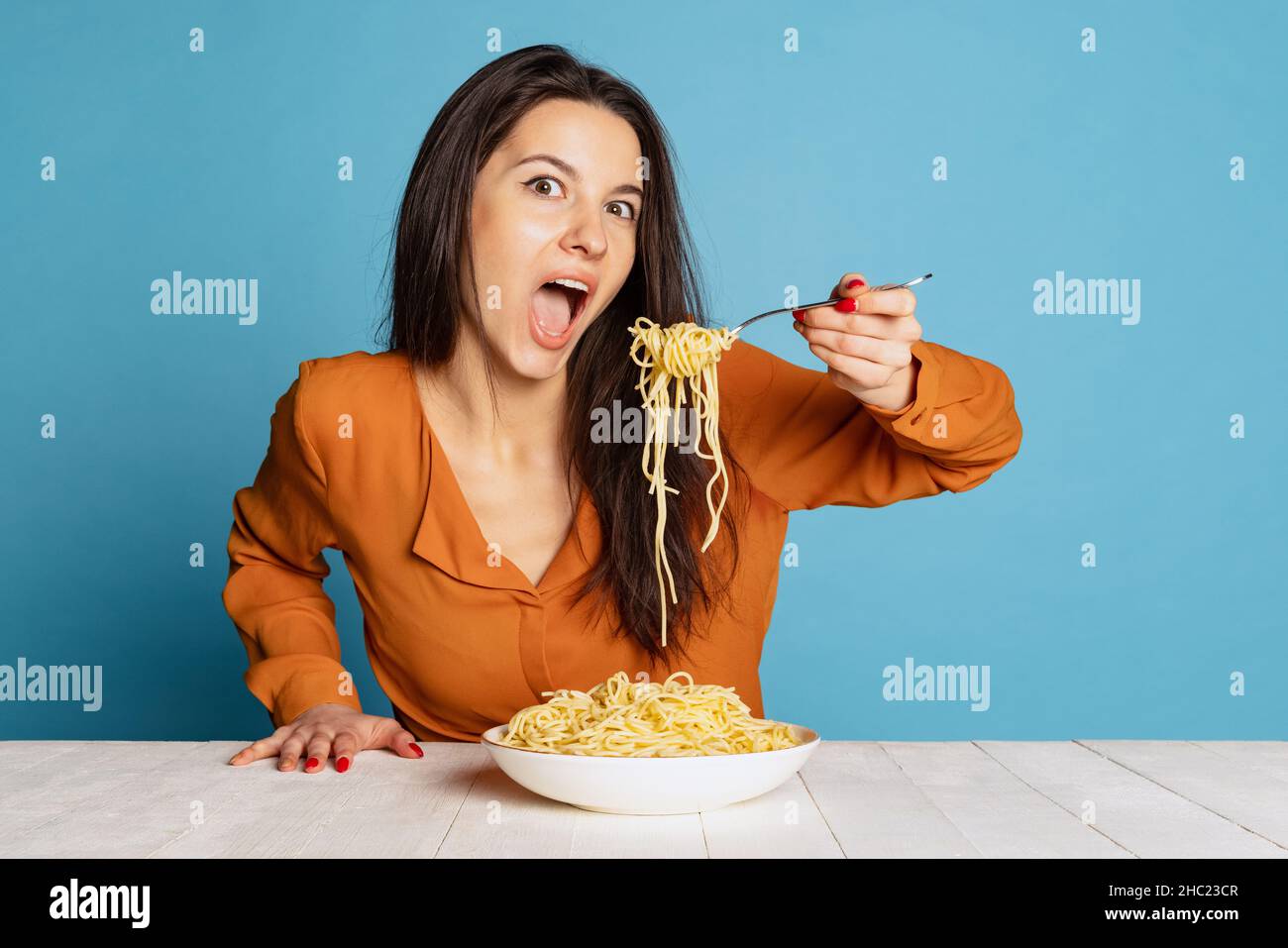 Schöne junge Mädchen essen köstliche italienische Pasta isoliert auf blauem Studio-Hintergrund. World Pasta Day Stockfoto