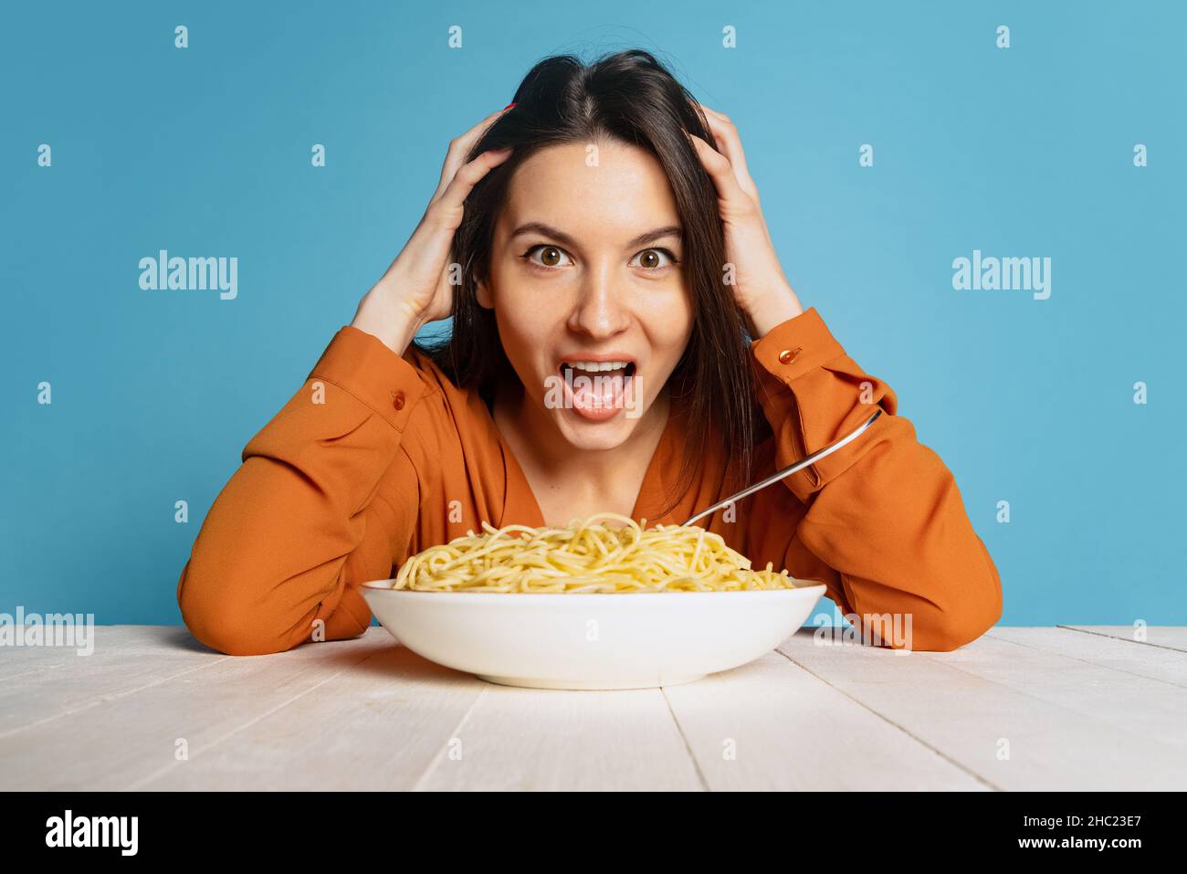 Schockiert junges Mädchen, das sich darauf vorbereitet, eine große Portion Nudeln auf blauem Studiohintergrund zu essen. World Pasta Day Stockfoto